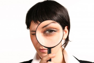 A professionally dressed woman holding a magnifying glass over her eye